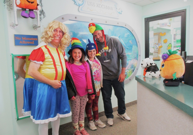 Dental office staff and children posing with colorful superhero mural decoration in pediatric dentistry clinic.