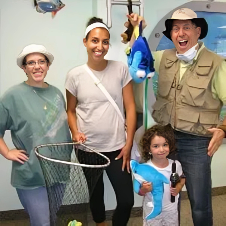Four people wearing safari hats hold fishing net indoors, dressed in themed costumes for children's dental office event.