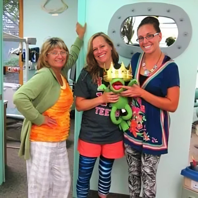 Three women holding toy soccer ball in colorful outfits in dental office reception area.