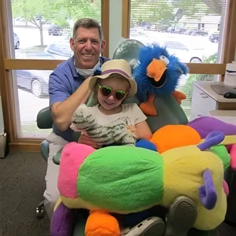 Man and child with colorful plush toy in dental office waiting room with windows.