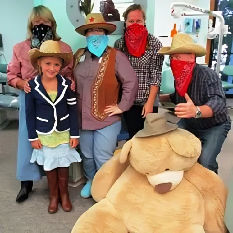 Group of people in Western costumes and cowboy hats posing together indoors at dental office.