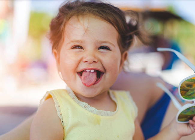 Happy toddler in yellow shirt sticking tongue out playfully outdoors.