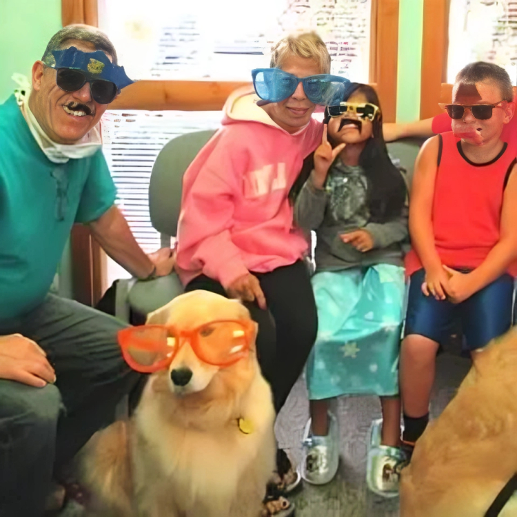 Children wearing novelty glasses pose with a dog wearing orange glasses in a dental office.