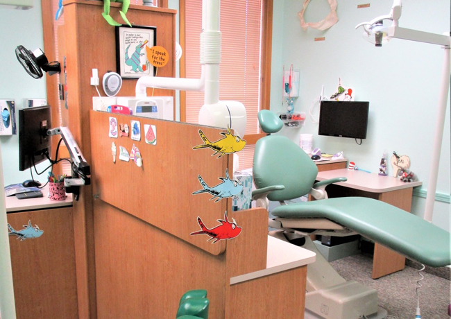 Colorful pediatric dental operatory with treatment chair, equipment, and child-friendly decorations on orange wall.