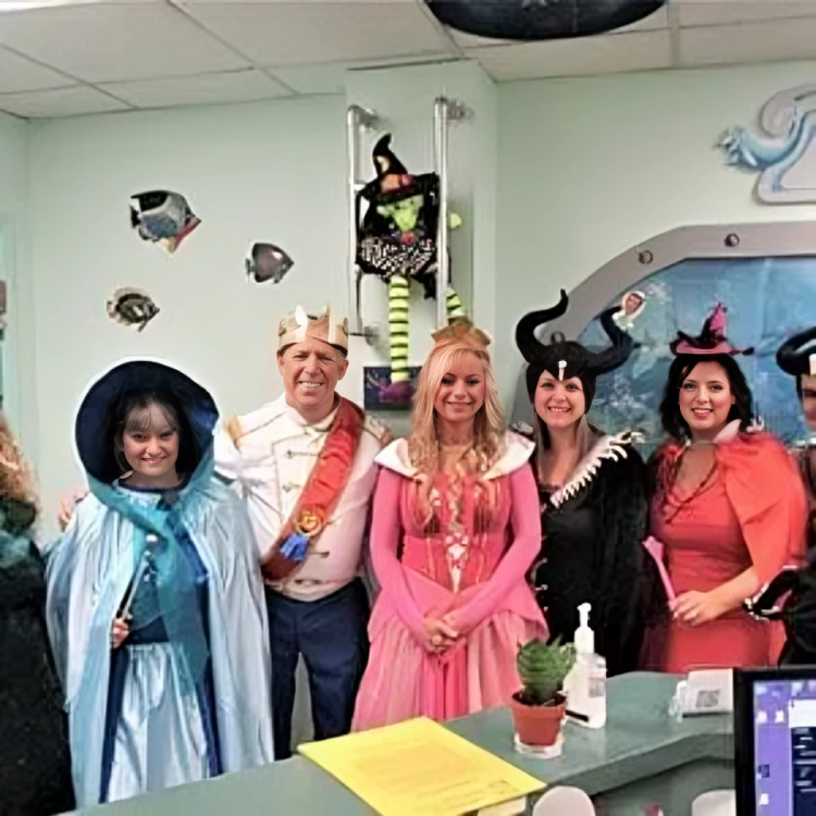 Dental office staff in Halloween costumes posing together in treatment room with decorations.