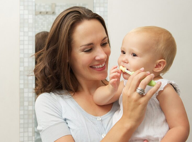 Mother and young child brushing teeth together in bathroom setting.
