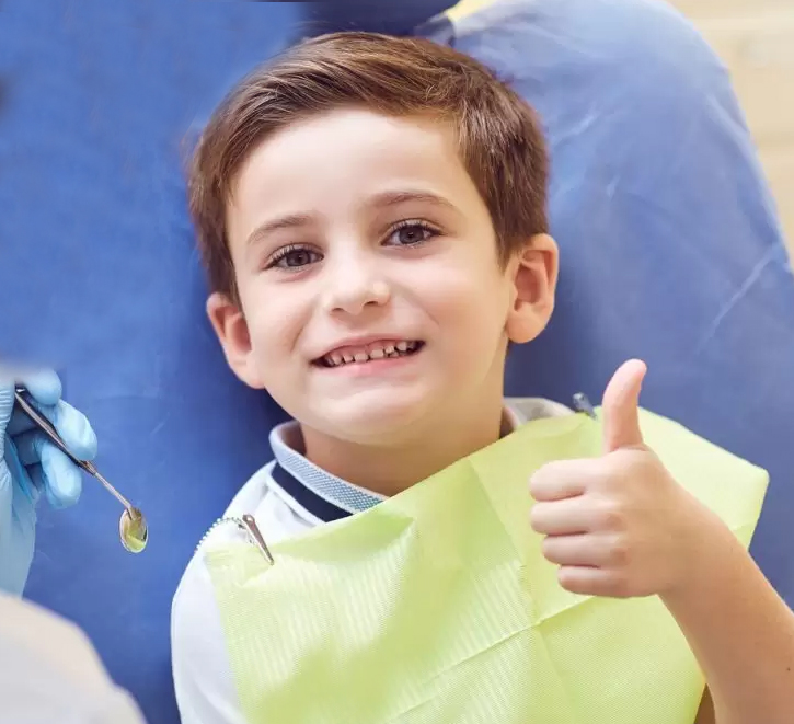 Young boy in yellow shirt giving thumbs up, smiling in dental office setting