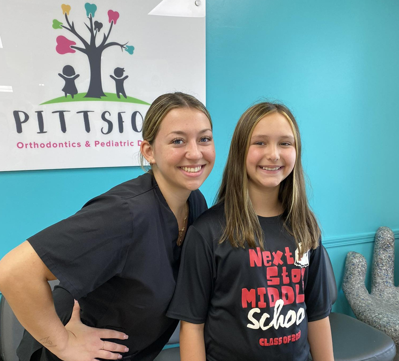 Two smiling staff members posing together at Pittsford Orthodontics & Pediatric Dentistry office.